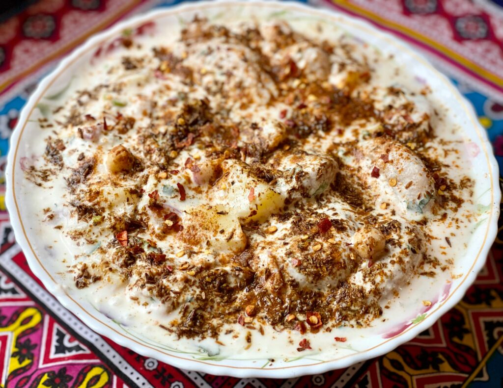 Delicious close-up of dahi vada garnished with spices and chutneys, traditionally served on a patterned cloth.