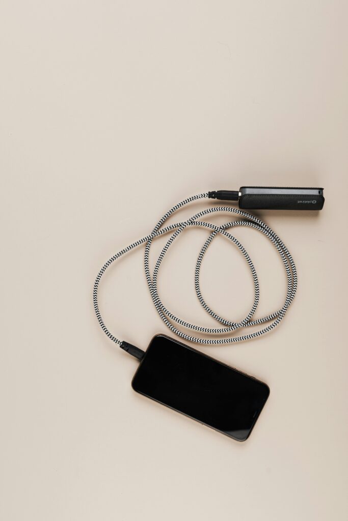 A mobile phone and power bank connected with a coiled cable on a beige background. Ideal for tech and lifestyle themes.