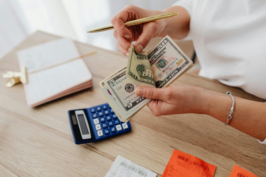 Woman counting cash with a calculator at a desk, managing finances.