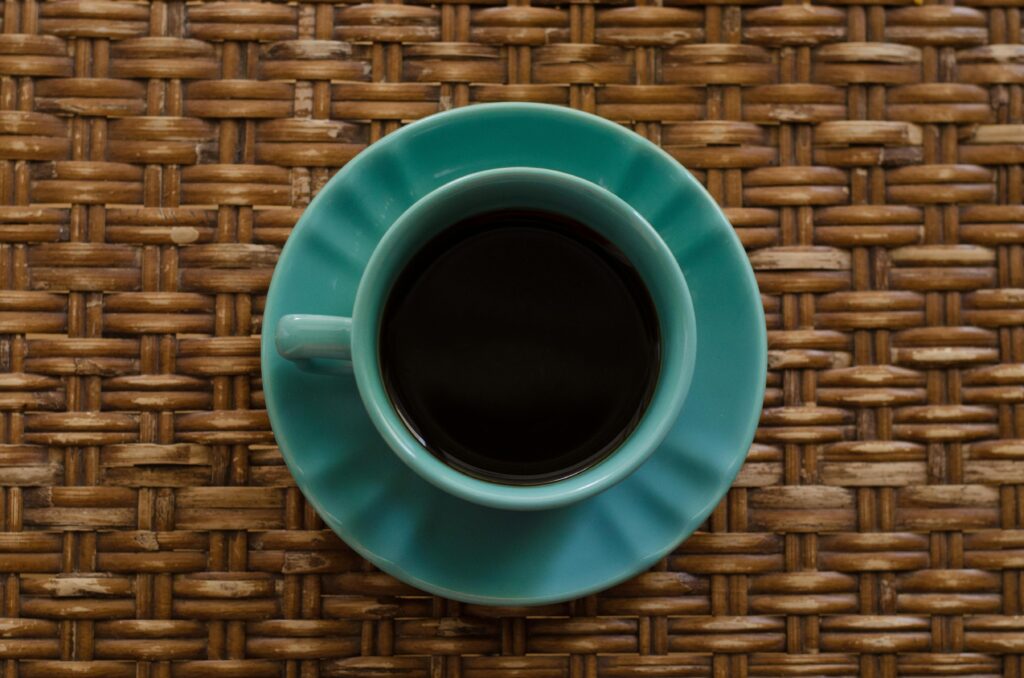 Ceramic turquoise cup of black coffee on a rattan mat, evoking a cozy coffee break.