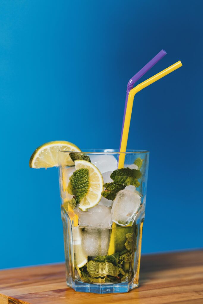 A vibrant mojito cocktail with lemon slices and mint leaves against a blue background, perfect for summer refreshment.
