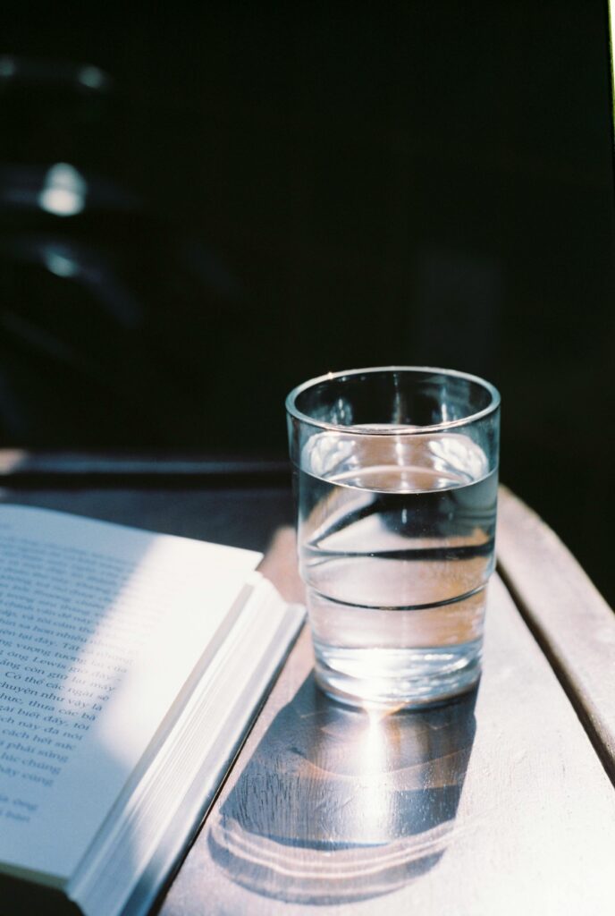 Glass of water and book on table in sunlight, creating a peaceful reading ambiance.