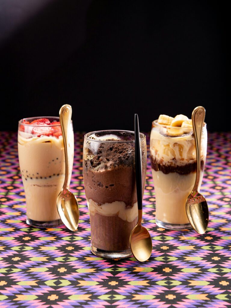 A colorful trio of milkshakes with toppings displayed on a vibrant patterned table.
